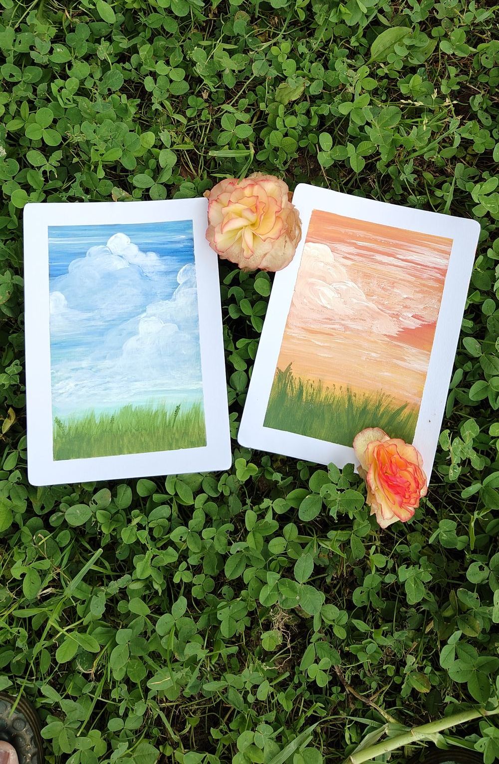 Two original gouache sky paintings resting in the grass with garden roses